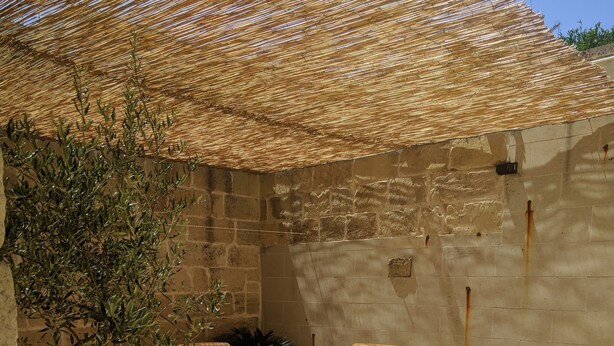 Un patio al aire libre con mobiliario de mimbre, una planta en maceta y un suelo de baldosas.