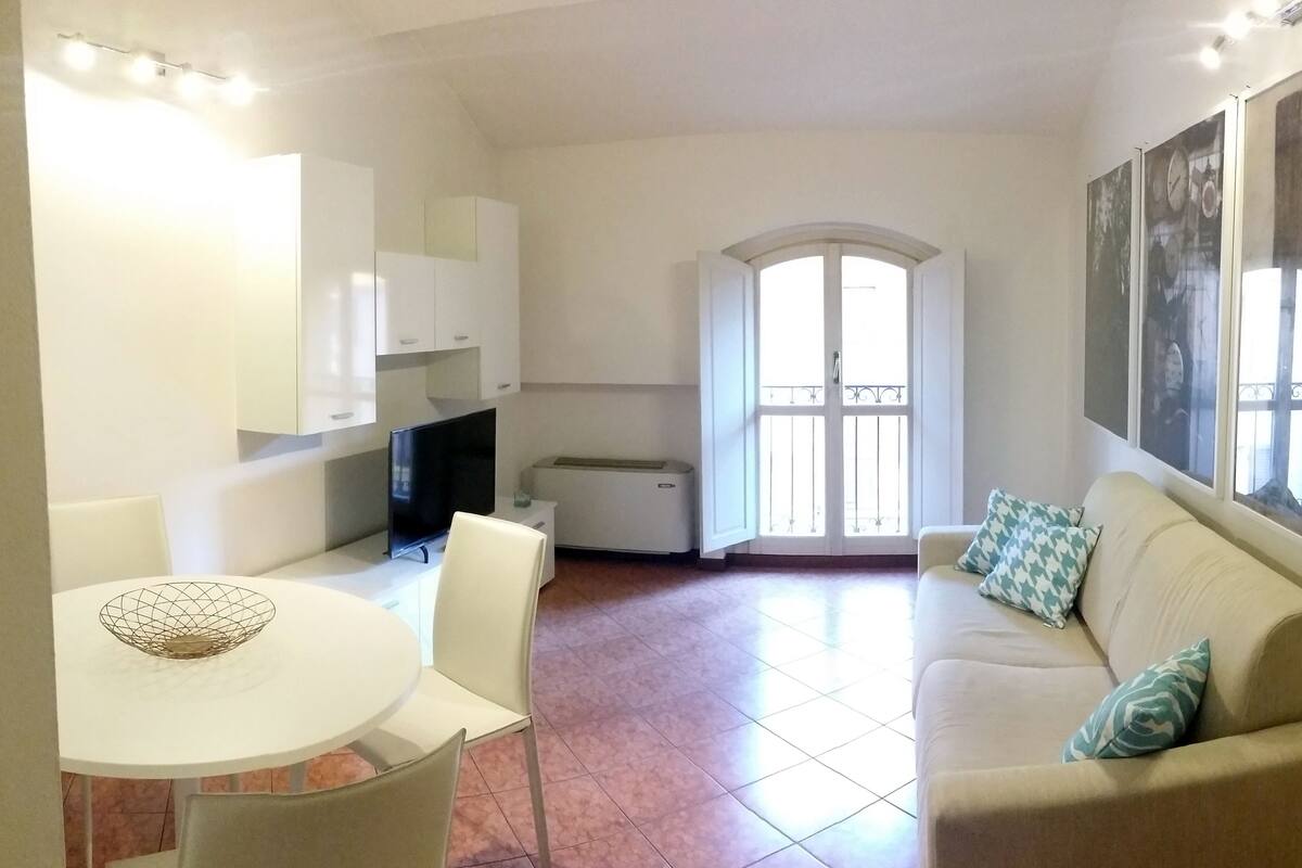 Un salon avec un canapé beige, une table à manger avec des chaises, un téléviseur et un coin cuisine avec des placards.