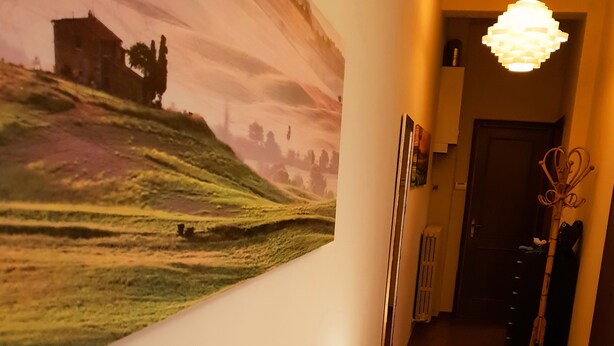 A hotel room with a large landscape painting on the wall, a white sofa, a small round table, and a radiator. - Mosaico Aparthotel (Modena)