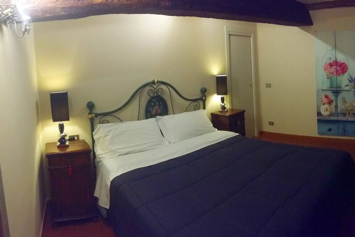 Une chambre à coucher avec un lit, des tables de chevet, une lampe, un tableau, une télévision et une poubelle.