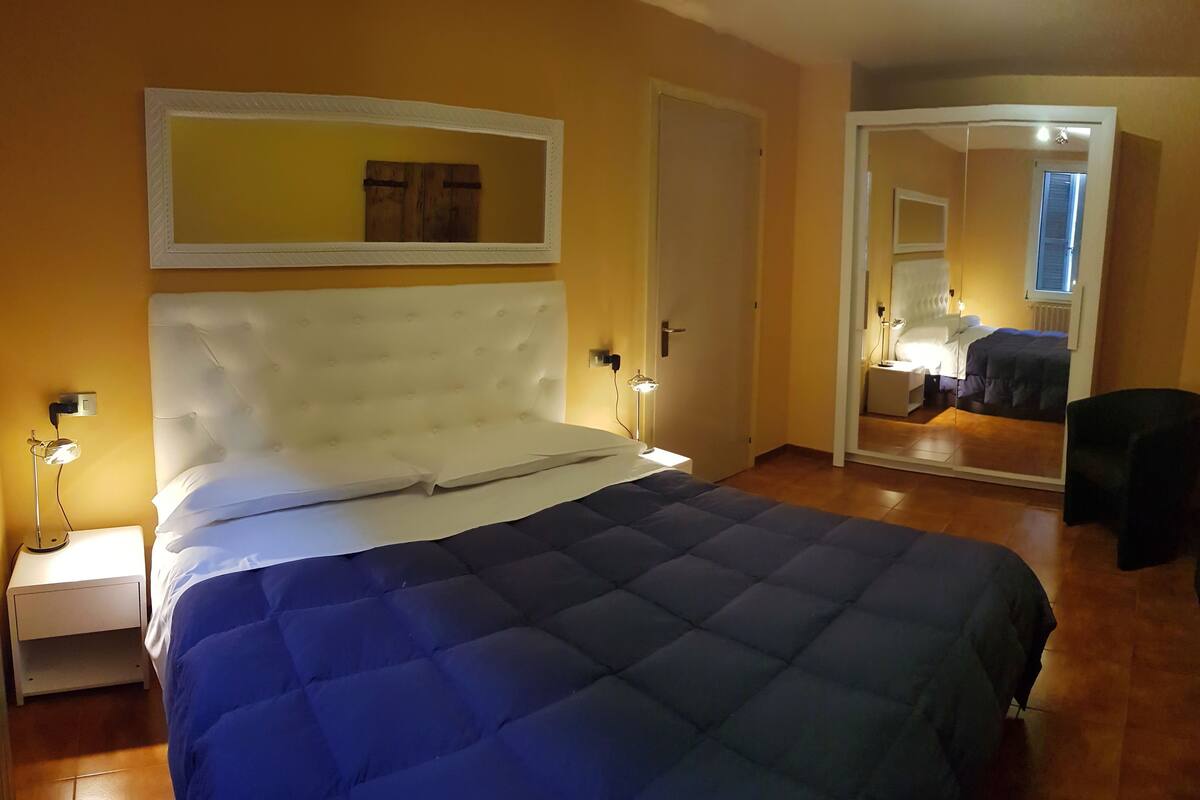 Une chambre à coucher avec un grand lit, une table de chevet avec une lampe, un miroir et une porte donnant sur une autre pièce.
