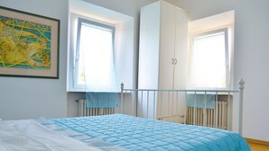 Quarto com cama, guarda-roupa e duas janelas.
