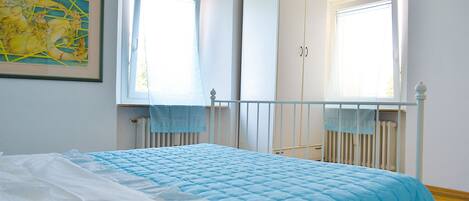 Un dormitorio con una cama, un armario y dos ventanas.