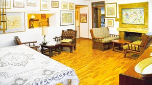 Uma sala de estar acolhedora com piso de madeira, lareira e diversas obras de arte emolduradas nas paredes.