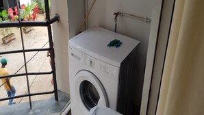 A compact laundry room with a washing machine and a drying rack. - Residence Fatny (Abidjan)