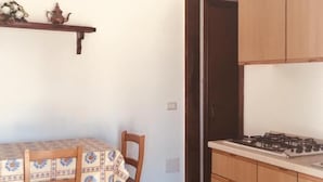 Een keuken met houten kastjes, een gasfornuis, een eettafel met stoelen en een plafondlamp.