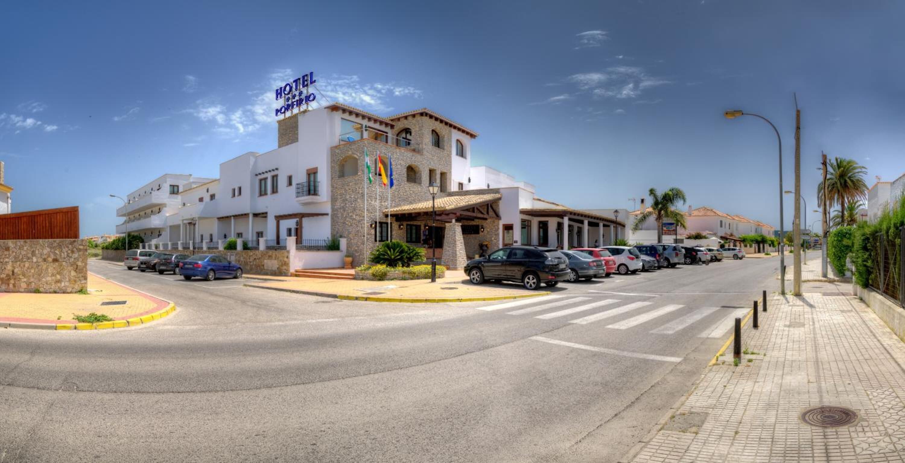 Un hotel con fachada blanca, varios balcones y un estacionamiento con varios coches.