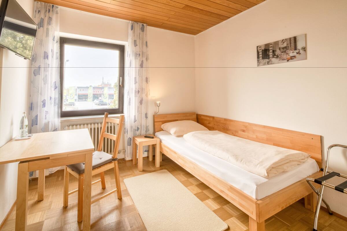 Une pièce avec un lit en bois, un bureau, une chaise et une fenêtre avec des rideaux.