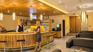Un espace bar avec un comptoir en bois, des tabourets de bar et un coin salon comprenant un canapé et des tables.
