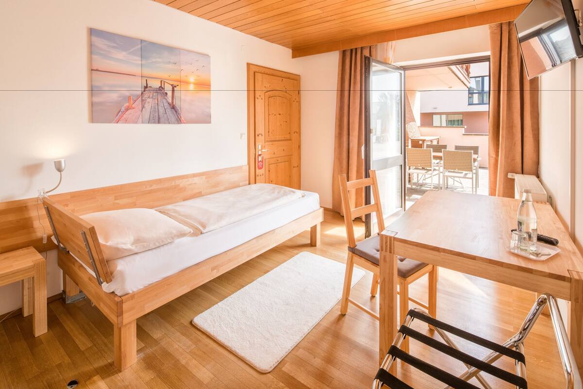 Une chambre avec un lit en bois, une petite table avec des chaises, une télévision et une vue sur l’extérieur.