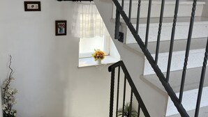 A staircase with a black railing, a small window with a white curtain, and a vase with flowers on the landing.
