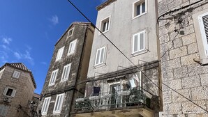 A narrow cobblestone street lined with historic stone buildings, featuring balconies with wrought iron railings and multiple windows with shutters.