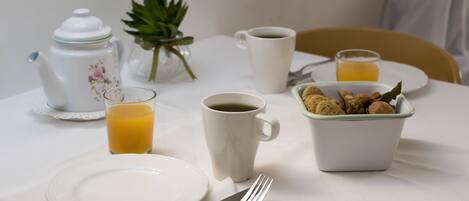 A breakfast table with a teapot, coffee cup, glass of orange juice, a bowl of cookies, and a plate.