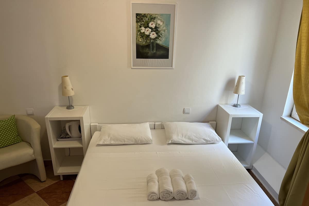 Een hotelkamer met een bed, twee nachtkastjes, een groen kussen, een lijst met een afbeelding aan de muur en een raam met gordijnen.