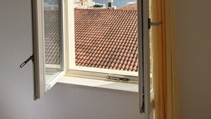 A window with a view of a coastal landscape, a tiled roof, and a curtain.