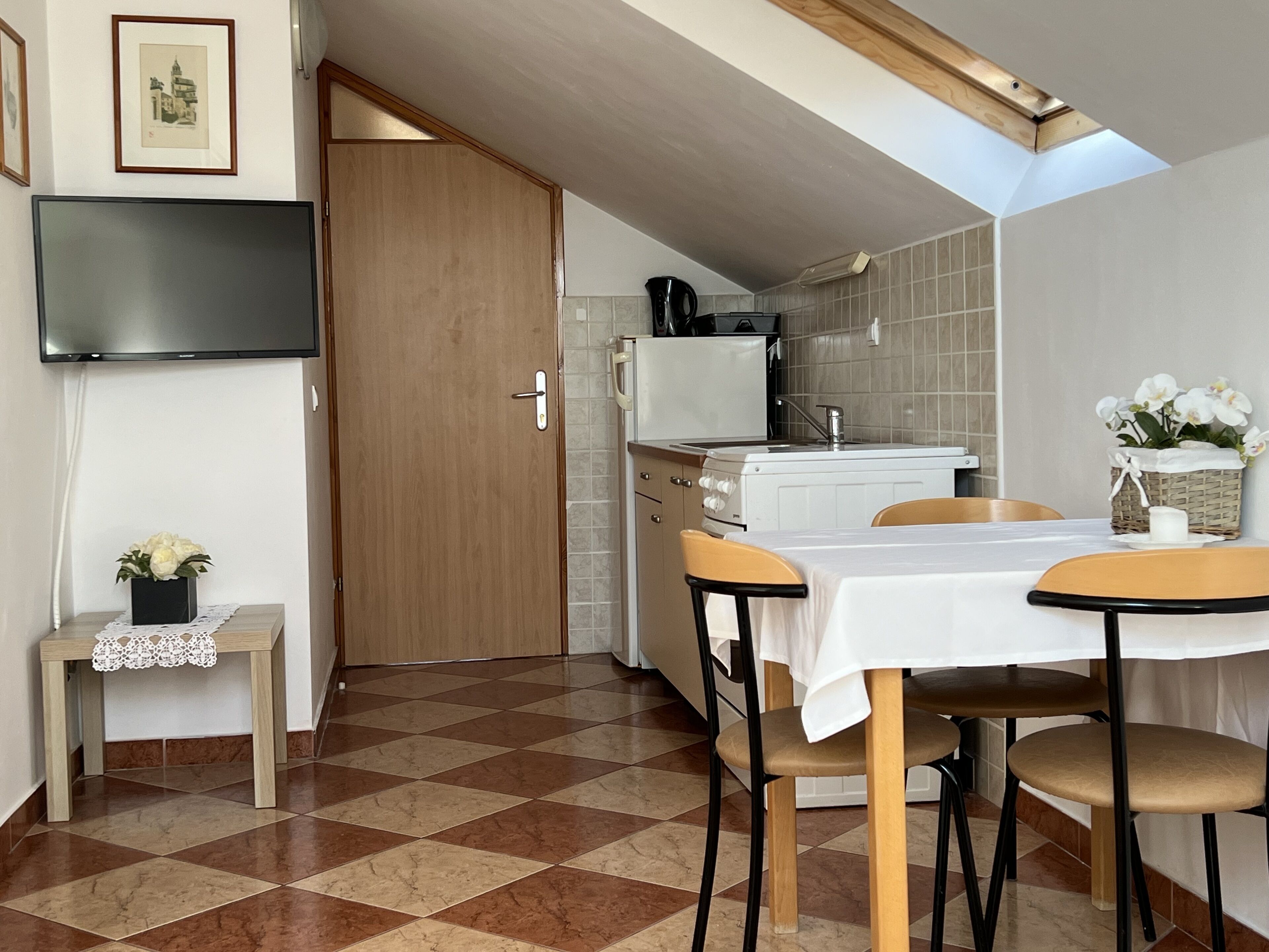A compact kitchen with a dining area, featuring a checkered floor, a white refrigerator, a stove, and a small table with chairs.