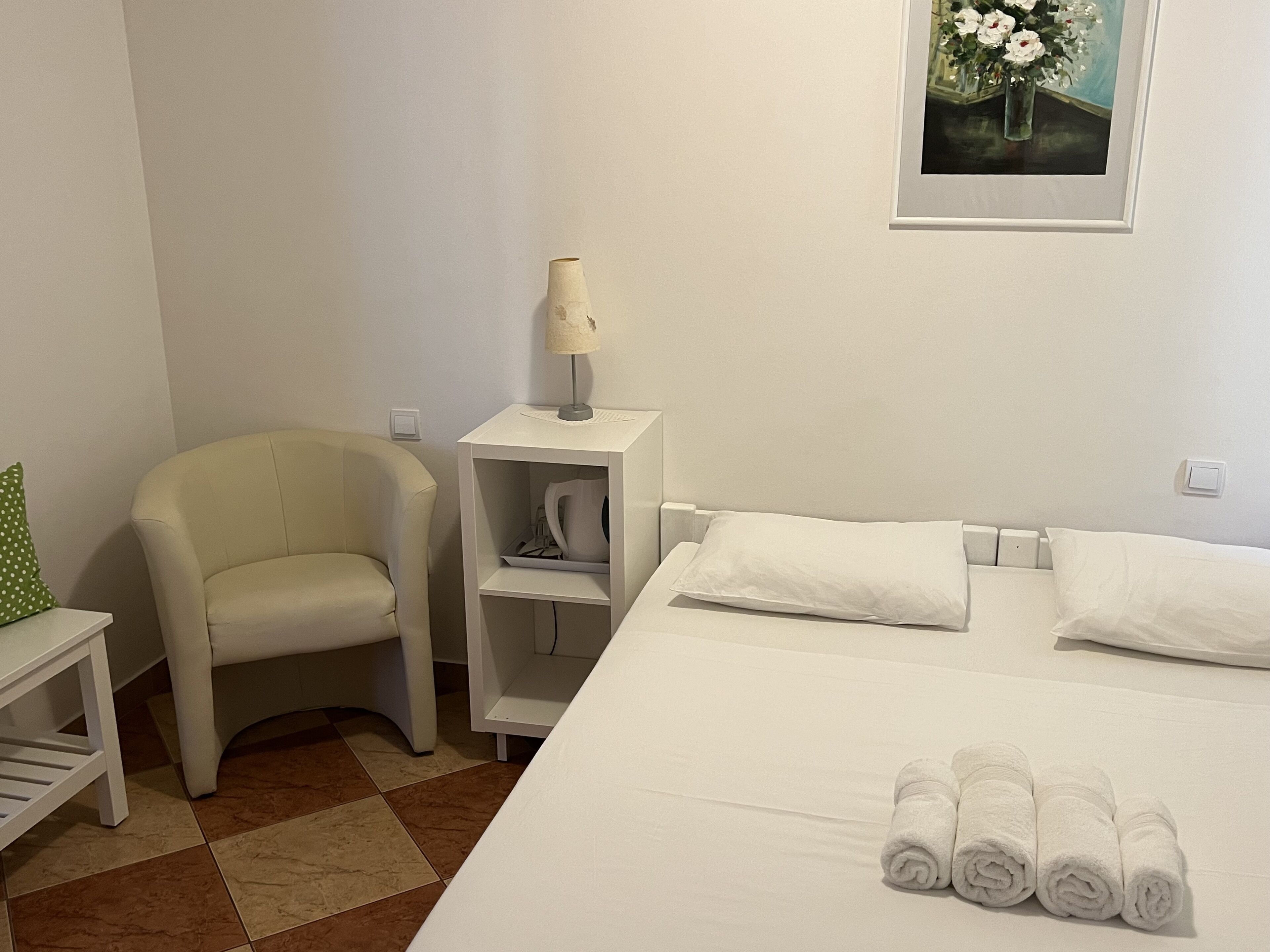 A hotel room with a bed, a chair, a nightstand with a lamp, and a painting on the wall.