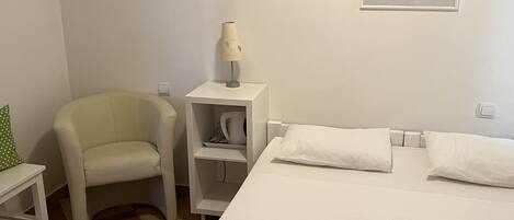 A hotel room with a bed, a chair, a nightstand with a lamp, and a painting on the wall.