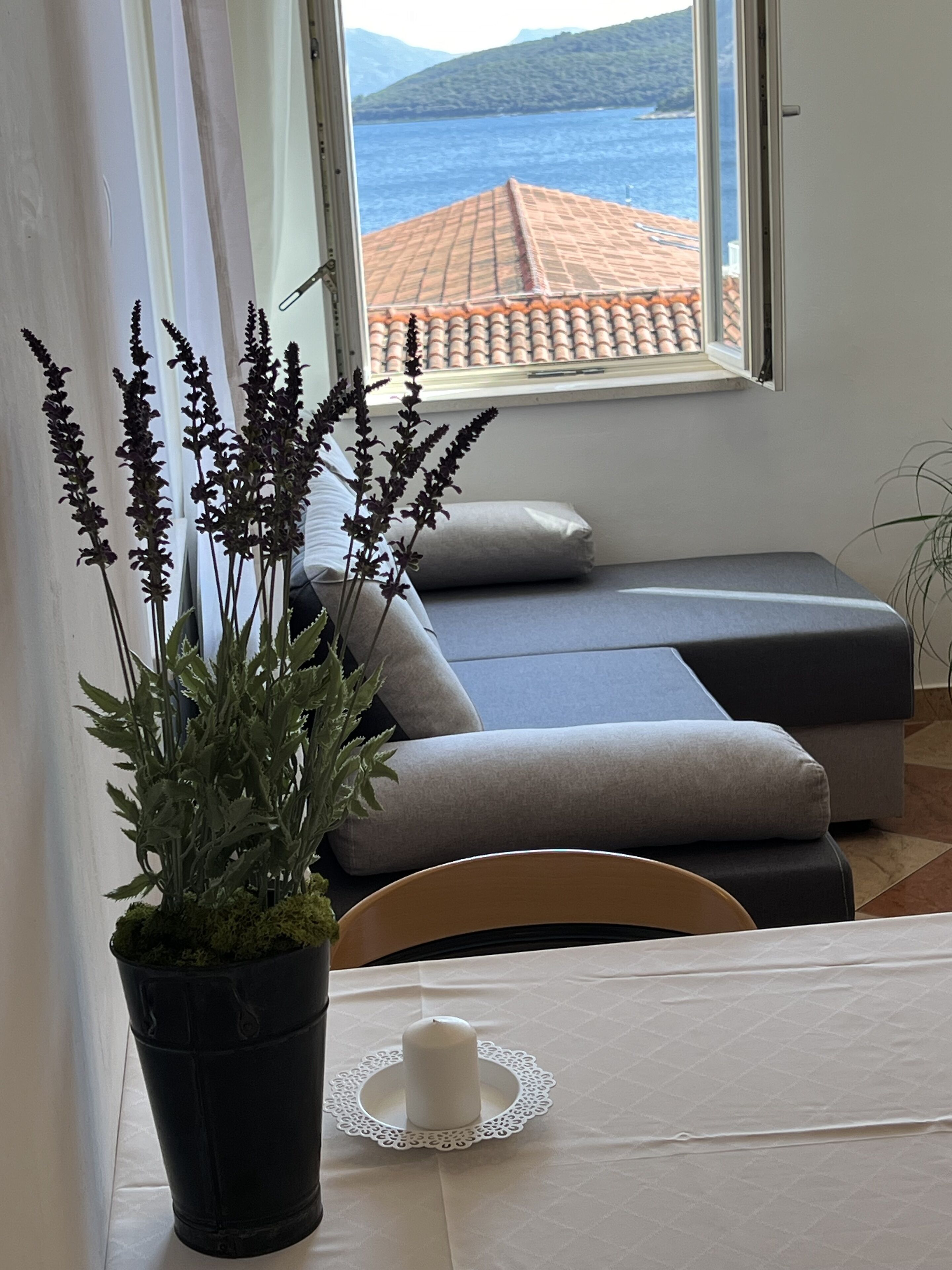 Una stanza accogliente con vista mare, una pianta in vaso, una candela bianca e un divano.