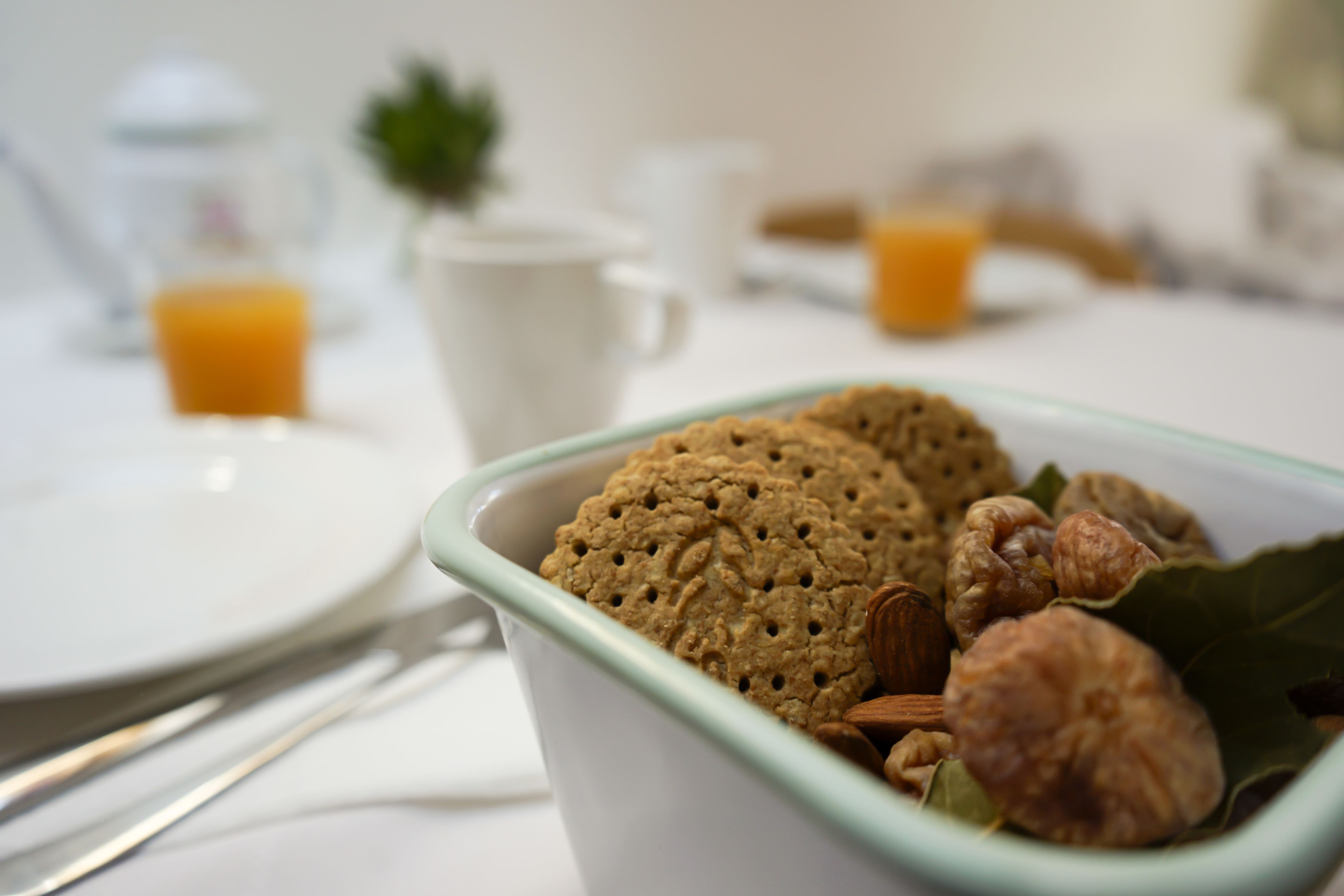 Un desayuno con un tazón de galletas y nueces, una taza blanca y un vaso de jugo de naranja sobre una mesa.