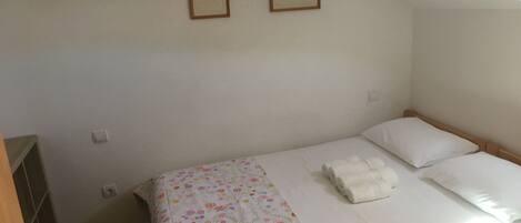 Un lit simple avec une couvre-lit à motifs floraux, deux tableaux encadrés au mur et une fenêtre laissant entrer la lumière naturelle.