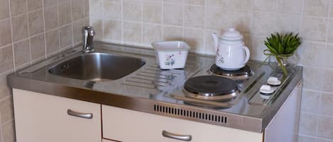 Una cocina con un lavamanos de acero inoxidable, una tetera blanca, un cuenco pequeño blanco y una planta en maceta.