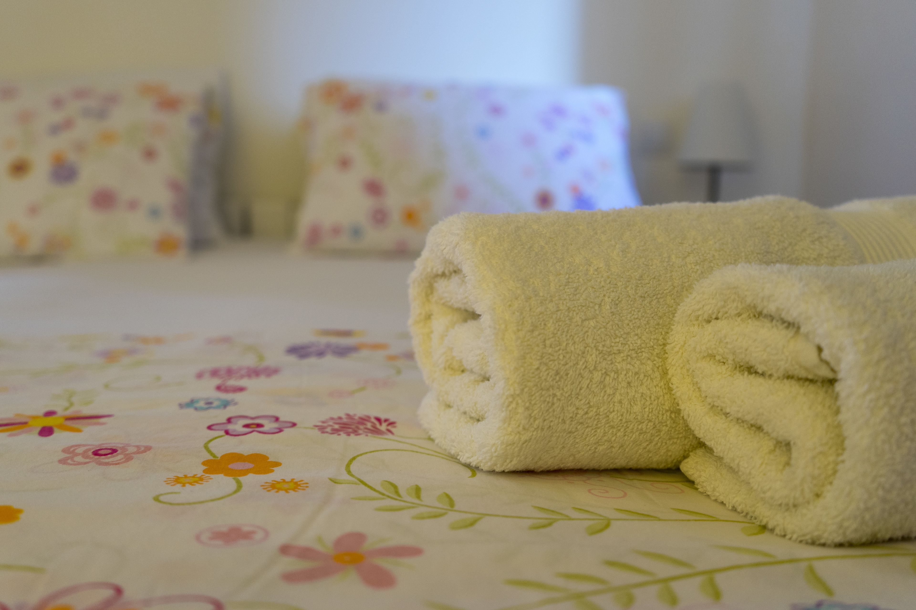 A neatly made bed with a floral-patterned bedspread and rolled towels.