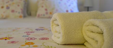 A neatly made bed with a floral-patterned bedspread and rolled towels.