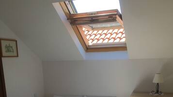 A bedroom with a skylight, a bed with white linens, and a bedside table with a lamp.