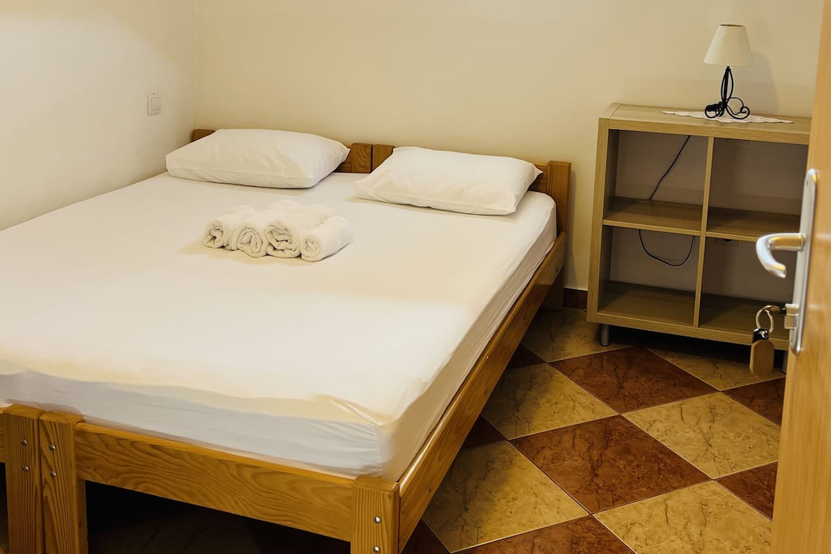 Een slaapkamer met een dakraam, een bed met witte lakens, een nachtkastje met een lamp en een betegelde vloer.