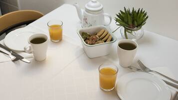 Et morgenbord med tallerkener, kopper, et tehus, en lille plante og en skål med nødder.