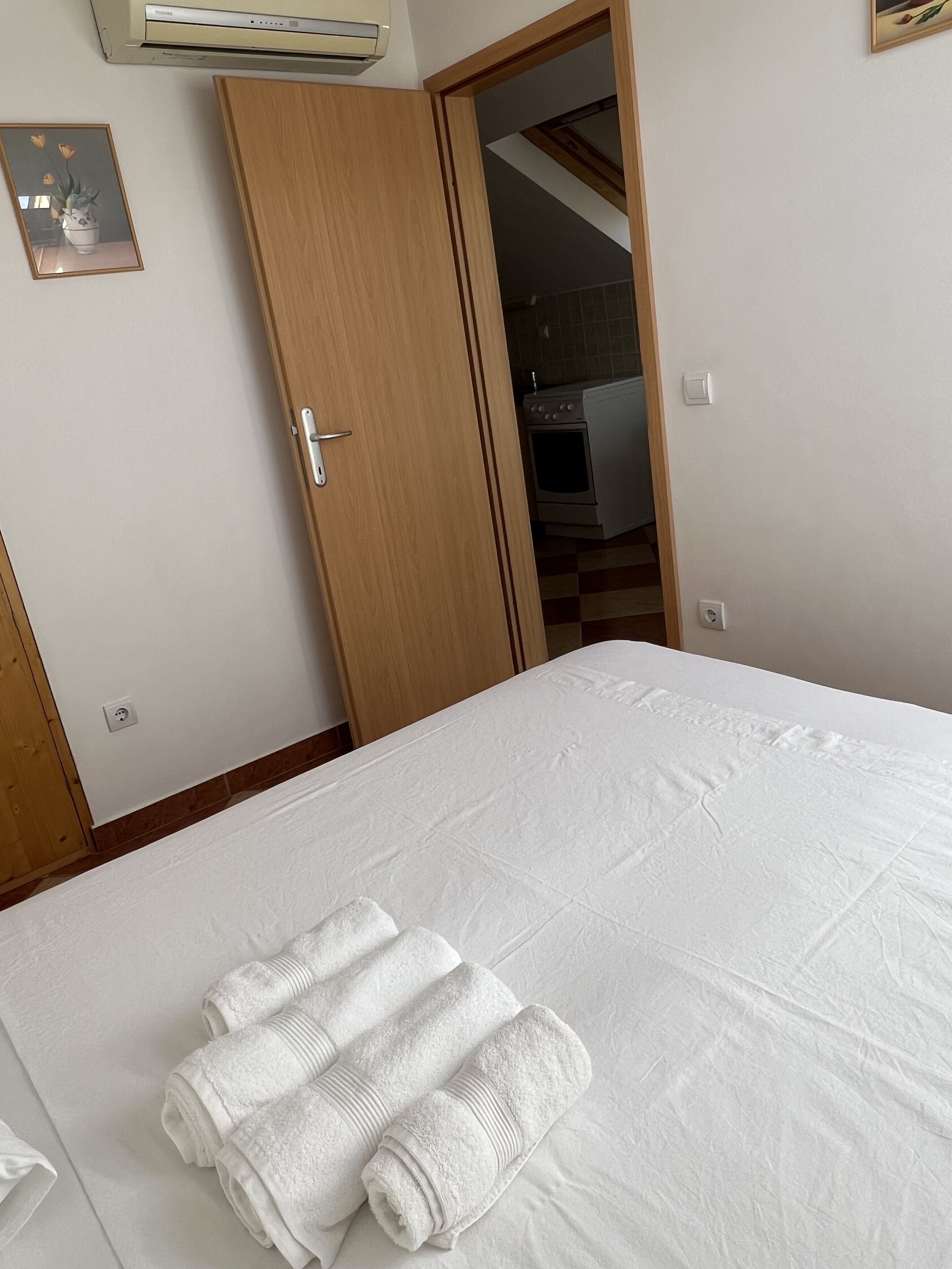 Une chambre d’hôtel avec un lit, une porte en bois et une cuisine visible à travers une porte ouverte.