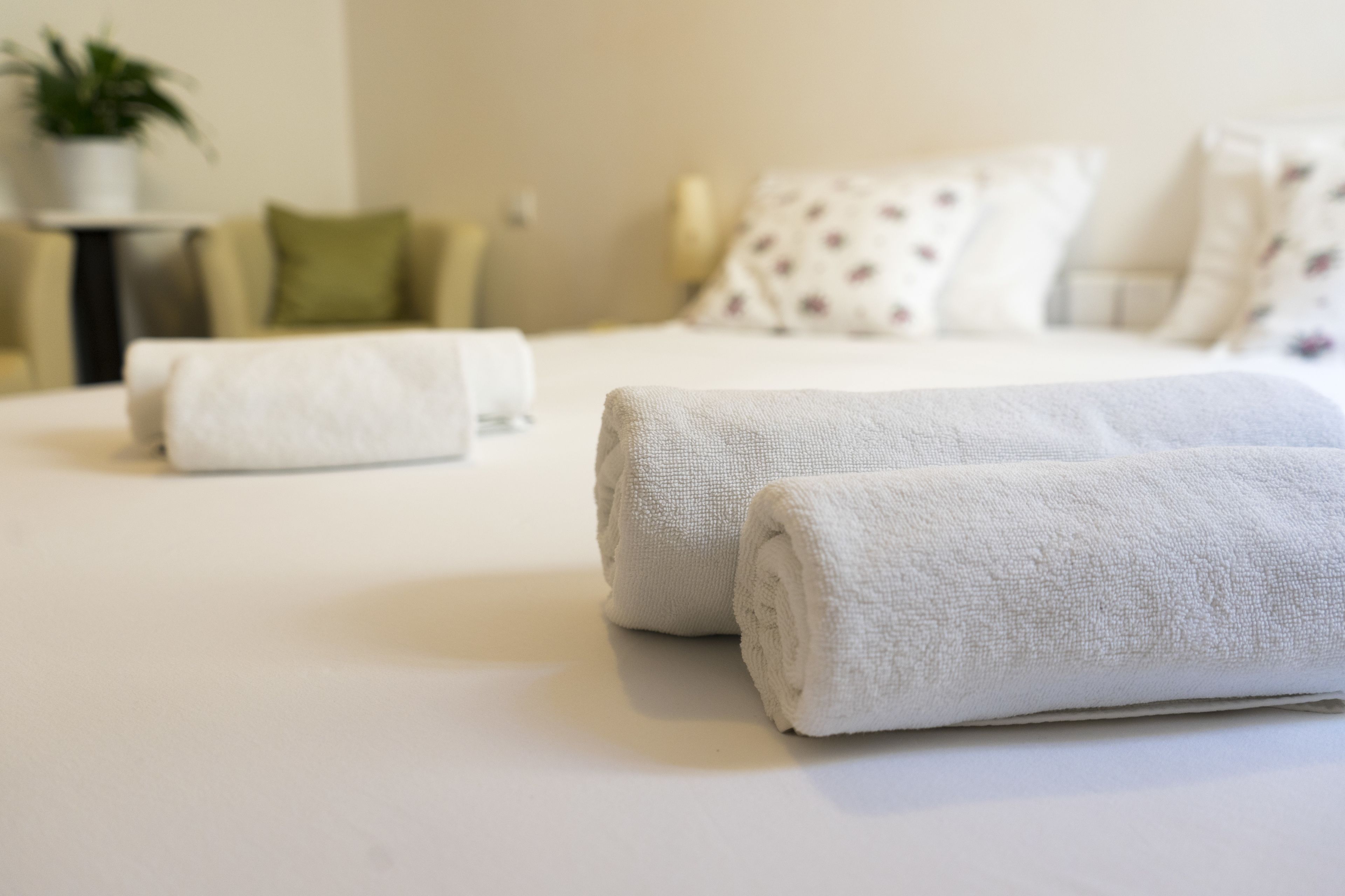 A neatly made bed with white linens and two rolled towels placed on it.