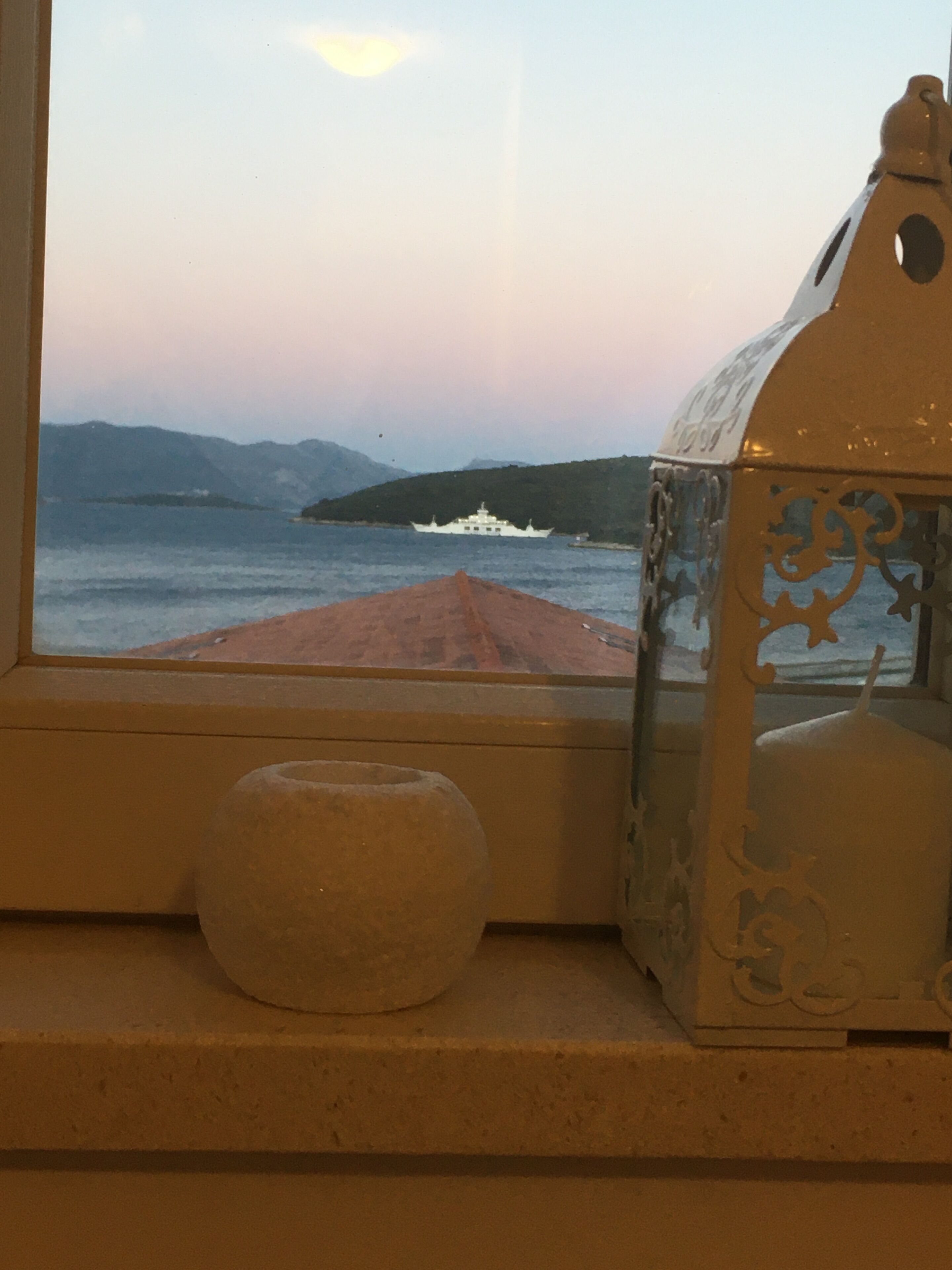 Blick durch ein Fenster mit einer verzierten Laterne und einer kleinen Vase auf der Fensterbank.