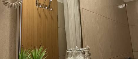A bathroom with a shower, a mirror, a towel rack, and a shelf with a potted plant.