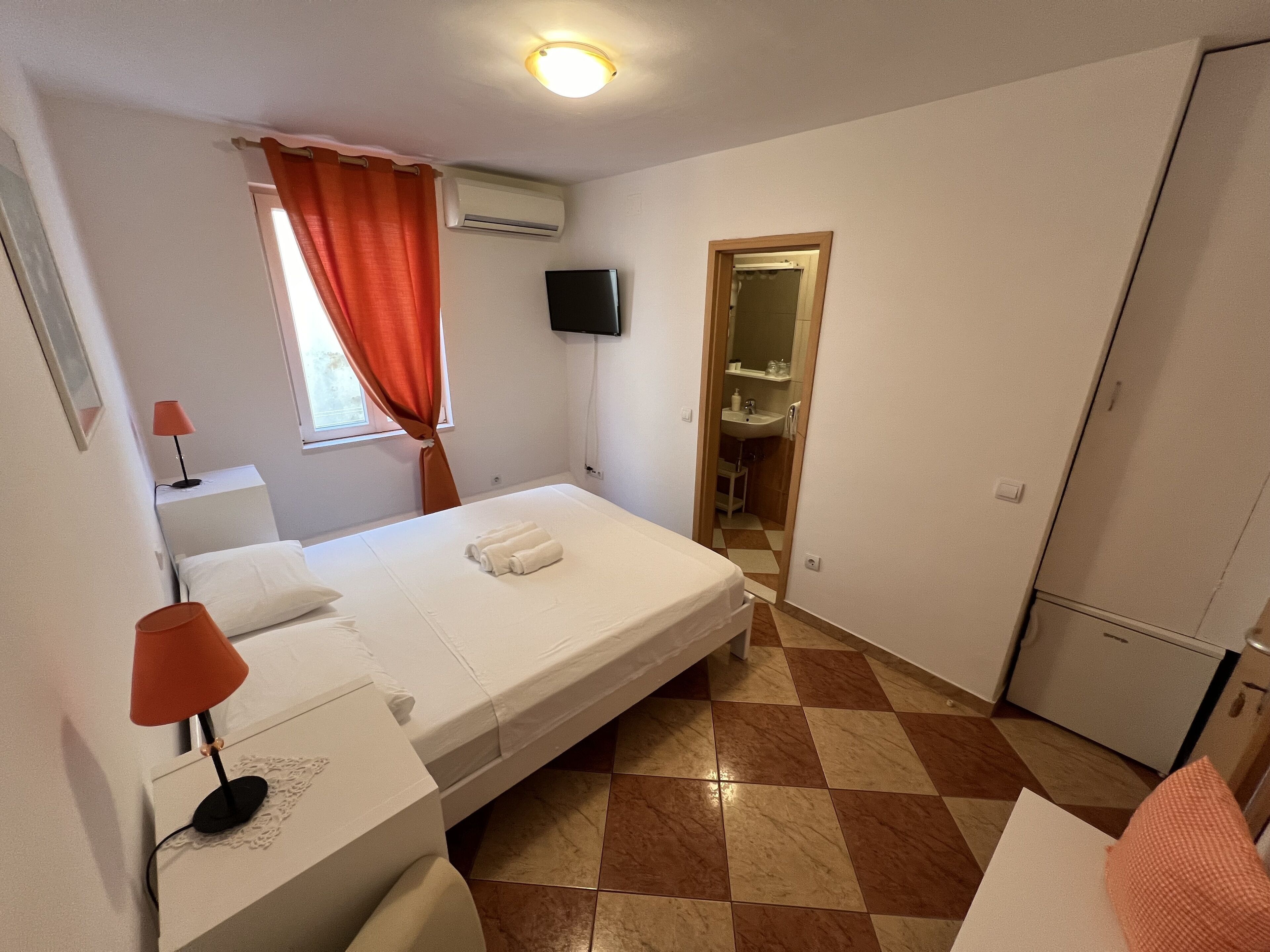 Una camera d'albergo con un letto, una scrivania, una sedia, una TV e un bagno visibile attraverso una porta aperta.