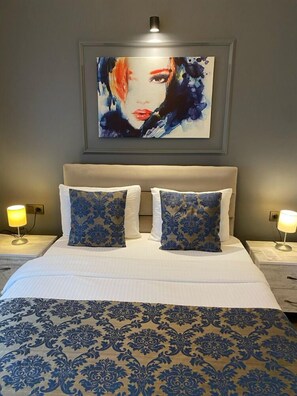 Relax in a spacious room with a large bed, two bedside tables, and a beautiful piece of artwork above.