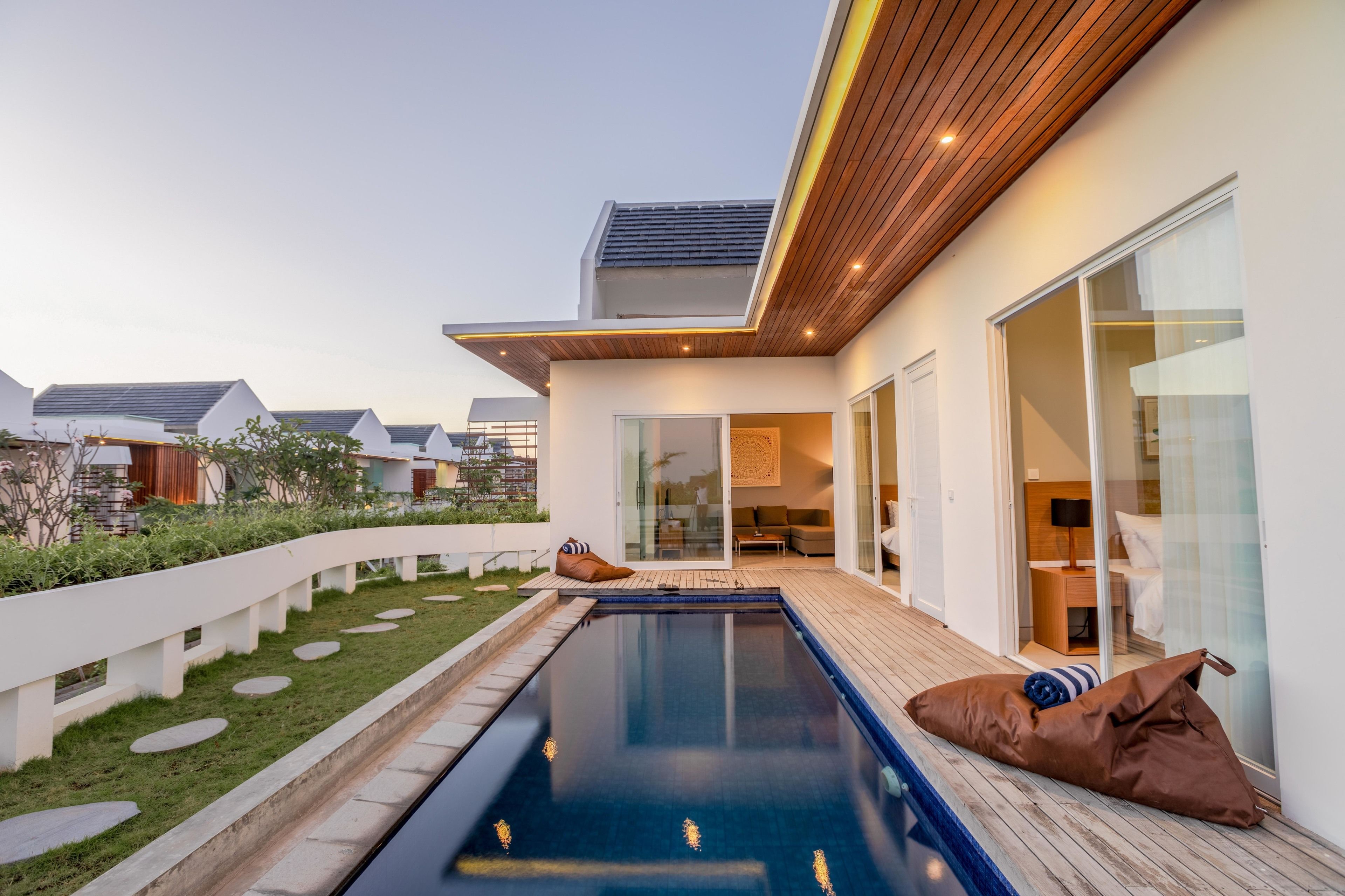 Ett modernt hus med en swimmingpool, ett trädäck och en glasdörr som leder in till ett vardagsrum.