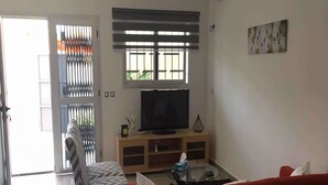 A living room with a sofa, a red couch, a TV on a wooden stand, and a window with blinds.