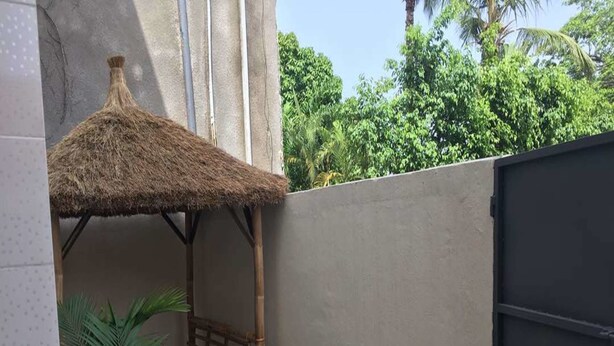 A small enclosed patio area with a thatched roof, a wooden bench, potted plants, and a tiled floor.