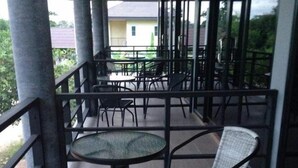 A covered outdoor seating area with tables and chairs, large windows, and a view of the surrounding area.