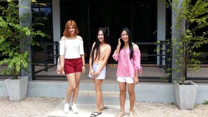 Three individuals standing in front of a building with a modern architectural design, featuring a concrete structure and glass windows.