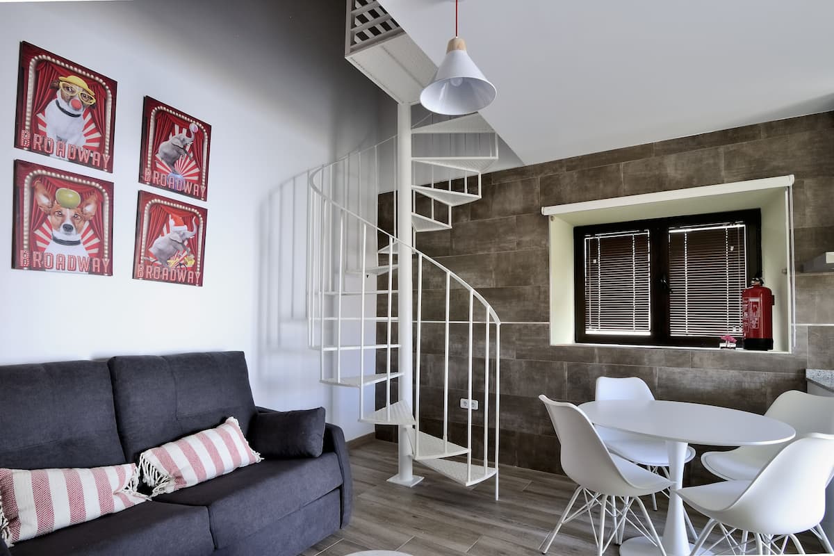 A modern living room with a grey sofa, white chairs, a white spiral staircase, and a window with blinds.