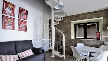 Un salón moderno con un sofá gris, sillas blancas, una escalera en espiral blanca y una ventana con persianas.