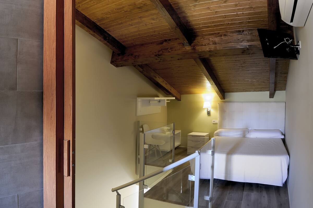 A bedroom with a wooden ceiling, a bed, a bedside table, and a small desk with a chair.