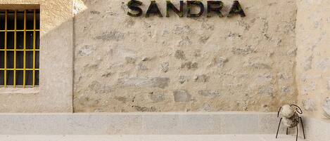 Une enseigne indiquant « PLAZA SANDRA » est fixée à un mur à texture, devant lequel se trouve une piscine carrelée.