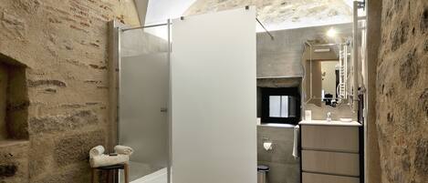 A bathroom with a glass shower enclosure, a wooden bench with towels, a sink, and a mirror.