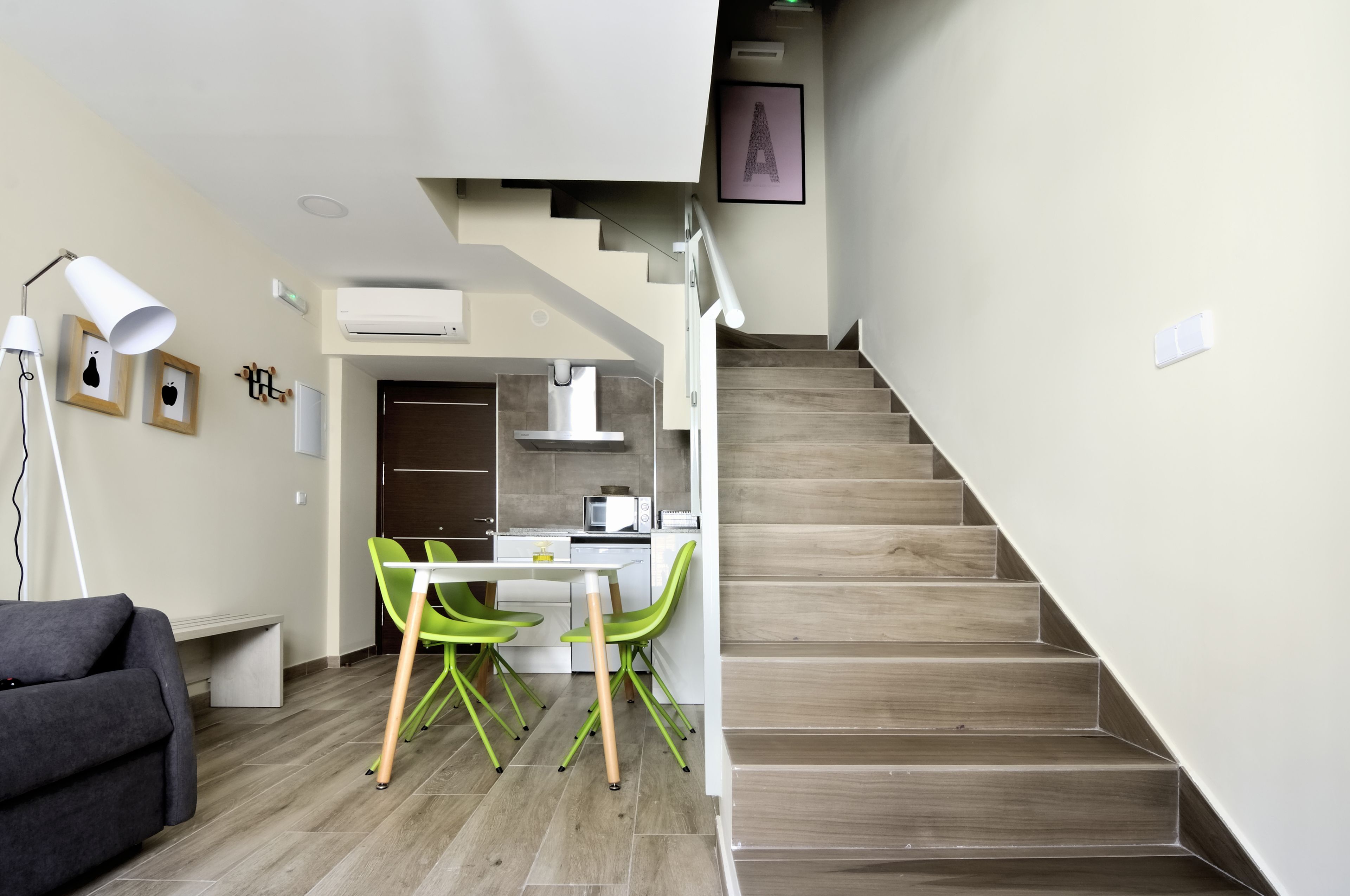 Un espacio habitable moderno con una escalera, un área de comedor con sillas verdes, un sofá gris y una mesa blanca.