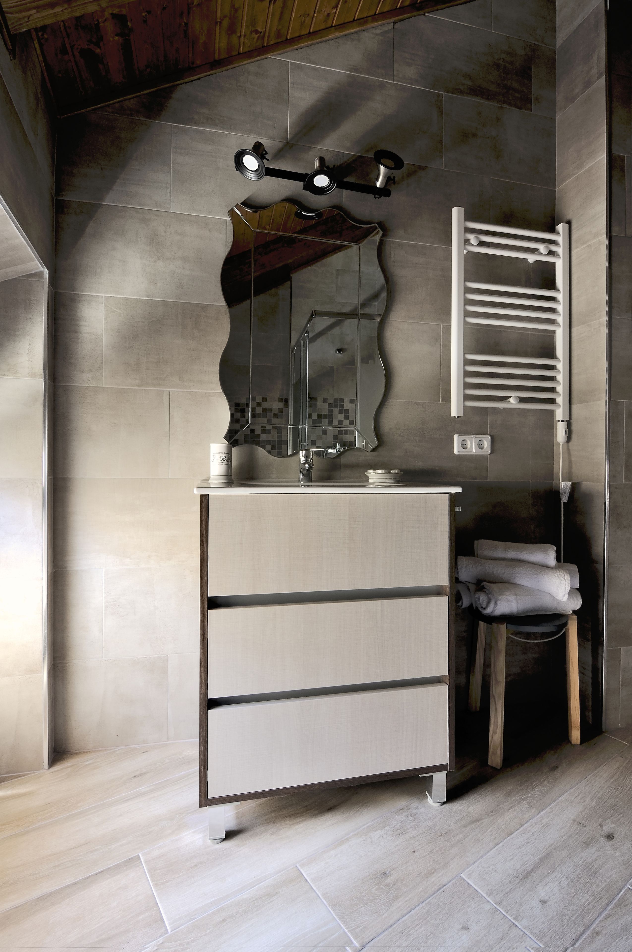 Une salle de bain équipée d’un meuble-lavabo, d’un miroir, d’un porte-serviettes et d’un tabouret en bois.