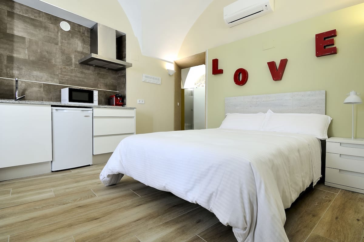 A modern hotel room with a bed, a kitchenette, and a wall with the word "LOVE" in large letters.